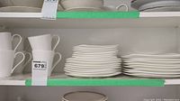 Shelving with stacked white mugs on left and stacks of white plates on right in kitchen environment
