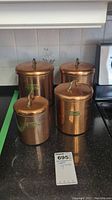 Four copper kitchen canisters arranged on countertop, viewed from front showing labels and brass handles on lids.