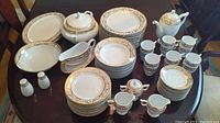 Photo showing full dinnerware set including plates, bowls, teacups, saucers, serving plates, tureen, teapot, gravy boat, creamers, sugar bowl, salt and pepper shakers on table.