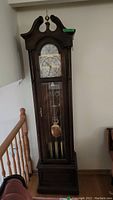 Full front view of the tall wooden grandfather clock with visible clock face and pendulum.
