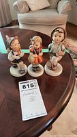 Photo of three Hummel children figurines on a wooden table showing front view and condition.