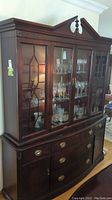 Front view of the Andrew Malcolm dining room hutch showing glass display cabinet with glassware inside and lower storage drawers and cabinets with brass handles.