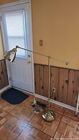 Adjustable brass floor lamp standing by door with adjustable arm and metal shade