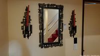 Front view of rectangular mirror with brutalist style frame and two matching sconces mounted on wall.