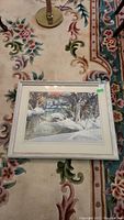 Framed watercolour painting of a winter stream scene on a floral carpet showing entire frame and glass.