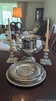 Full set of silver plated candlesticks, urn, and trays arranged on dining table.