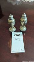 Two sterling silver salt and pepper shakers shown front view with lot tag labeled 'sterling'.