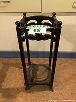 Full frontal view of the dark wood umbrella stand showing its open-frame design, turned finials, and metal drip tray base.
