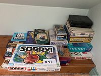 Photo showing stacked boxed games including Sorry!, Sequence, Pictionary, Cranium, Boggle, Guessures, and others