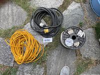Photo showing three electrical wiring items on stone surface: yellow extension cord, black extension cord with yellow plug, and spool of white wire.