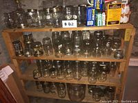 Wood shelving unit displaying a large collection of clear glass mason jars of different sizes and styles.