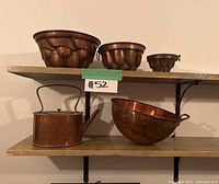 Shelf view showing all six copper kitchenware items: three copper molds, one mixing bowl, one copper kettle/watering can.