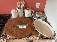 Photo of kitchen countertop showing wooden cutting board, ceramic baking dish, pitcher, utensil holder, canister, and Wedgwood stoneware items.