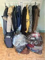 Whole lot showing leather and faux fur jackets and vests on a clothing rack, purple suitcase and multiple plastic bags filled with clothes and bags, indicating variety and quantity.