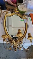 Front view of the gilt oval mirror with three sconce arms laid flat on table