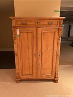 Front view of closed pine cabinet showing drawer and double doors with carved detailing