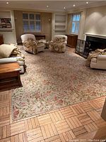 Living room setting with carpet laid on parquet floor, surrounded by furniture including sofas and fireplace.