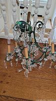 Full view of the green painted metal chandelier with multiple arms and hanging crystal prisms on wood floor.