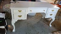 Full front and side view of white painted wood desk showing drawers and brass handles