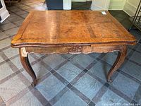 Full view of rectangular antique dining table with burl-wood veneer top and curved legs.