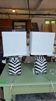 Pair of two zebra pattern ceramic and glass base table lamps with white fabric square lampshades on green table.