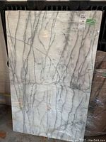 Photo of front side of a white marble slab with gray natural veining, wrapped in plastic.