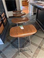 Angled view of four stools in lineup, showing bentwood seats and metal frames