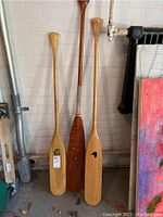Three wooden canoe paddles leaning against a brick wall