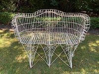Front view of white painted metal patio love seat showing scrollwork, lattice seat, and curved arms and backrest