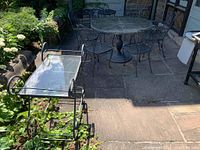 Outdoor view showing two-tier metal trolley with glass shelves and patio table with chairs in background