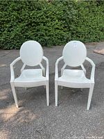Front view of two white Louis Ghost chairs placed side by side outdoors showing their oval backrests and armrests.