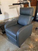Grey PVC leather covered recliner chair shown from front angle on concrete floor with exercise treadmill nearby.