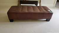 Front and top view showing full rectangular brown leather ottoman with button-tufted top and four short square legs.