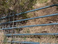 Stack of galvanized steel fence panels with four horizontal rails leaning against brush
