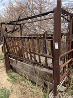 Full view of the cattle squeeze chute showing metal tubing frame and wood base panels outdoors.