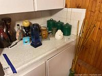Photo shows a collection of Asian-inspired ceramic containers, vases, glassware, and decorative items on a countertop.