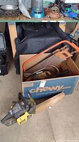 Photo showing McCulloch chainsaw resting on floor next to a box containing multiple hand saws.