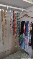 Photo shows several gold-tone costume jewelry necklaces and assorted scarves on hangers.