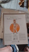 Photo showing vintage Sunkist Orange Juice advertisement featuring a child holding a glass and a large orange illustration.