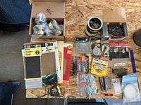 Photo of assorted 3M sandpaper sheets, keyed door knobs and locks, tape measure, screws, bolts, package hinges, hooks, hanging wire and Conoco pocket cutter laid out on wood surface.