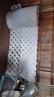 White lattice panels stacked against wooden wall alongside large plastic trough container.