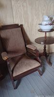 Antique East Lake style rocker with upholstered arms, back and seat, wood frame, next to three-tier round wood table with Johnson Bros pitcher and basin on top