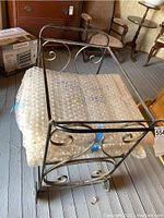 Photo of full tea cart showing metal frame with scroll design and bubble wrap on glass top.