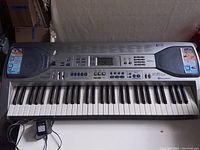 Full front and top view of Casio LK90 keyboard showing keys, speakers, control panel, and power adapter.