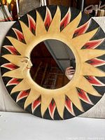 Full frontal photo of circular sun mirror with distinct red, gold, black sun rays and crescent moon face.