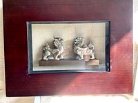 Front facing photo of wooden display case with glass front showing two vintage silver-tone Fu Dog statues inside on a wooden base.