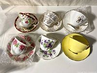 Top-down view of all six teacup and saucer sets, showing floral, patterned, and yellow designs.