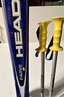 Close-up photo showing the blue Head Carve 6 ski and yellow handles of the poles.