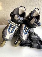 Pair of K2 inline skates in grey, blue, and black, shown with laces, Velcro straps, and ratchet buckles. Wheels visible on bottoms.