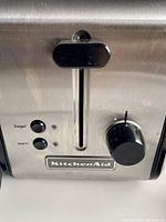 Close-up photo of the front panel of the toaster showing control buttons (bagel and warm) and dial with KitchenAid logo.